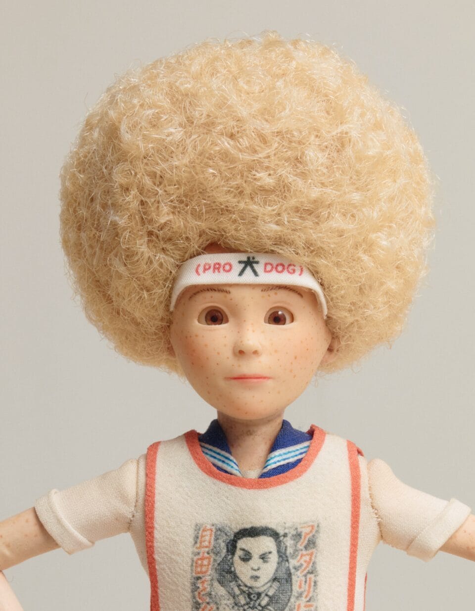 a blond doll with an afro, wearing a headband and a white jersey