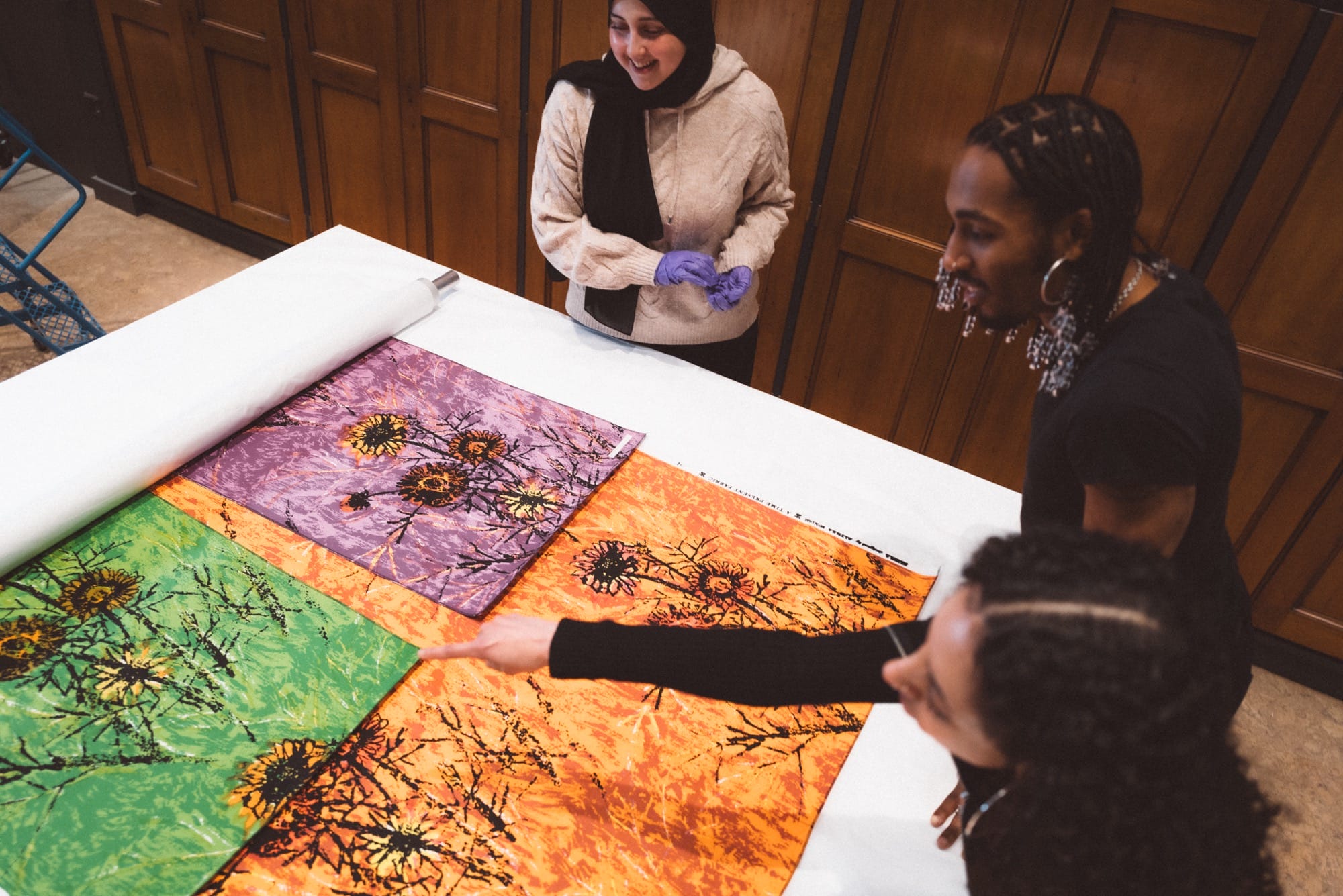 three people sit around a table, looking at textiles from a museum collection