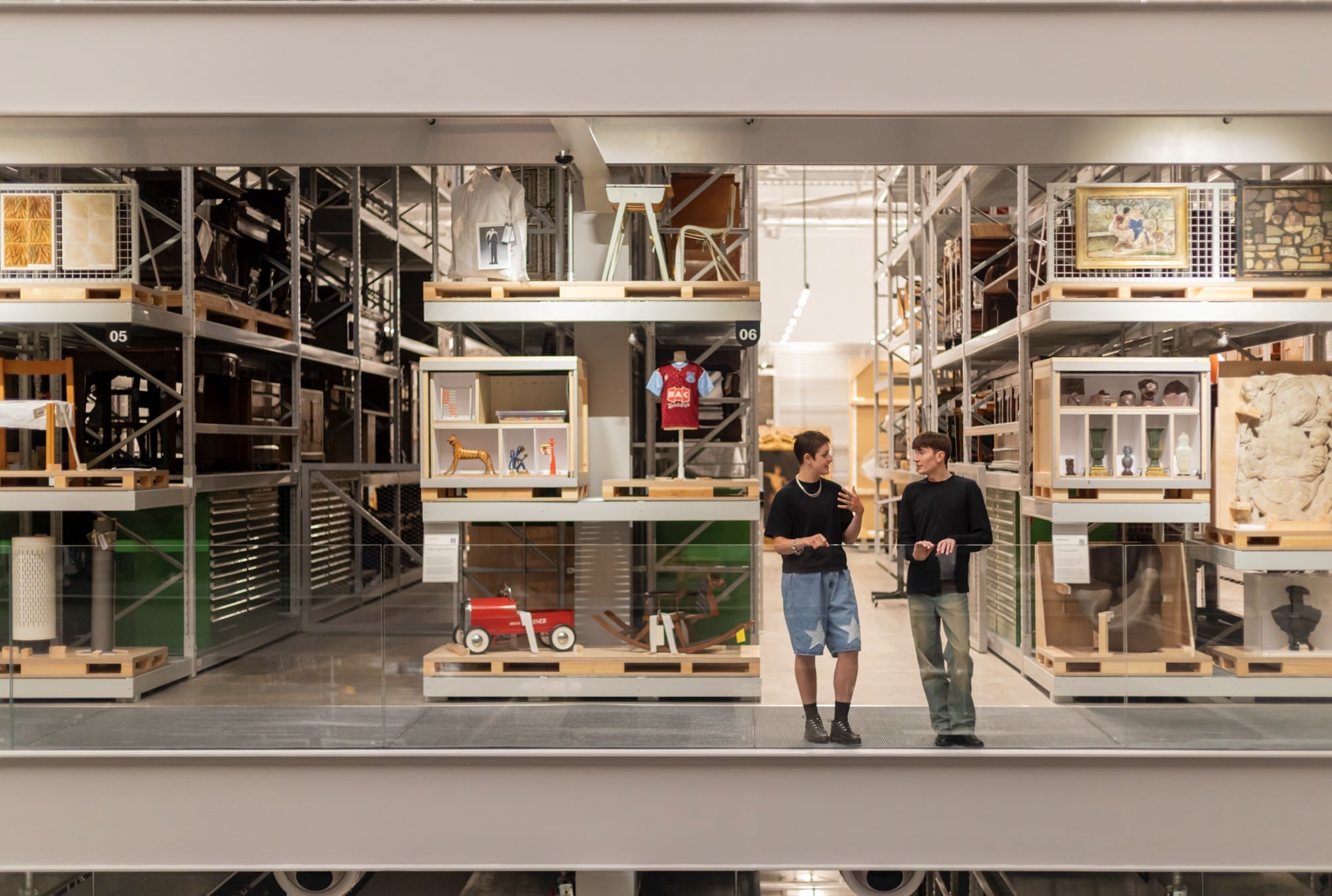two people stand talking on a mezzanine inside a large museum storehouse